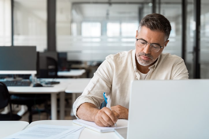 Photo of a man writing on a piece of paper in office space.