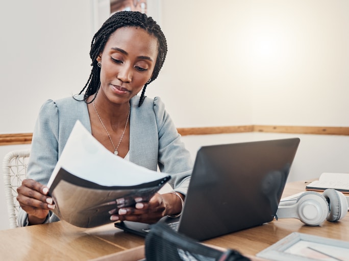 Photo of woman reading documents with a laptop open infront of her